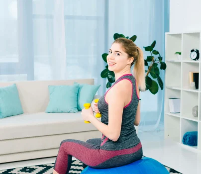 smiling-young-woman-sitting-fitness-ball-exercising-with-yellow-dumbbells